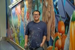 Alex Chiu stands in front of his mural in the north tunnel of the Portland International Airport
