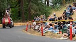 A rider on the Team Dragon soapbox car waves to the crowd going into turn 10 on the course at the 2026 Adult Soapbox Derby at Mt. Tabor Park in Portland, Ore., on Aug. 15, 2026. The soapbox derby had 42 different teams, with each made of two or three riders, and at least one person to push the soapbox at the start of the race.