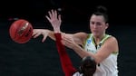 A basketball player dressed in white, yellow and green Oregon Ducks uniform passes a ball around a player in a red and white South Dakota uniform.