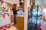 A man stands in his kitchen, with several water jugs sitting on shelves.