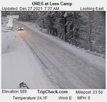 Snow or ice can be seen on a road surrounded by snow and trees.