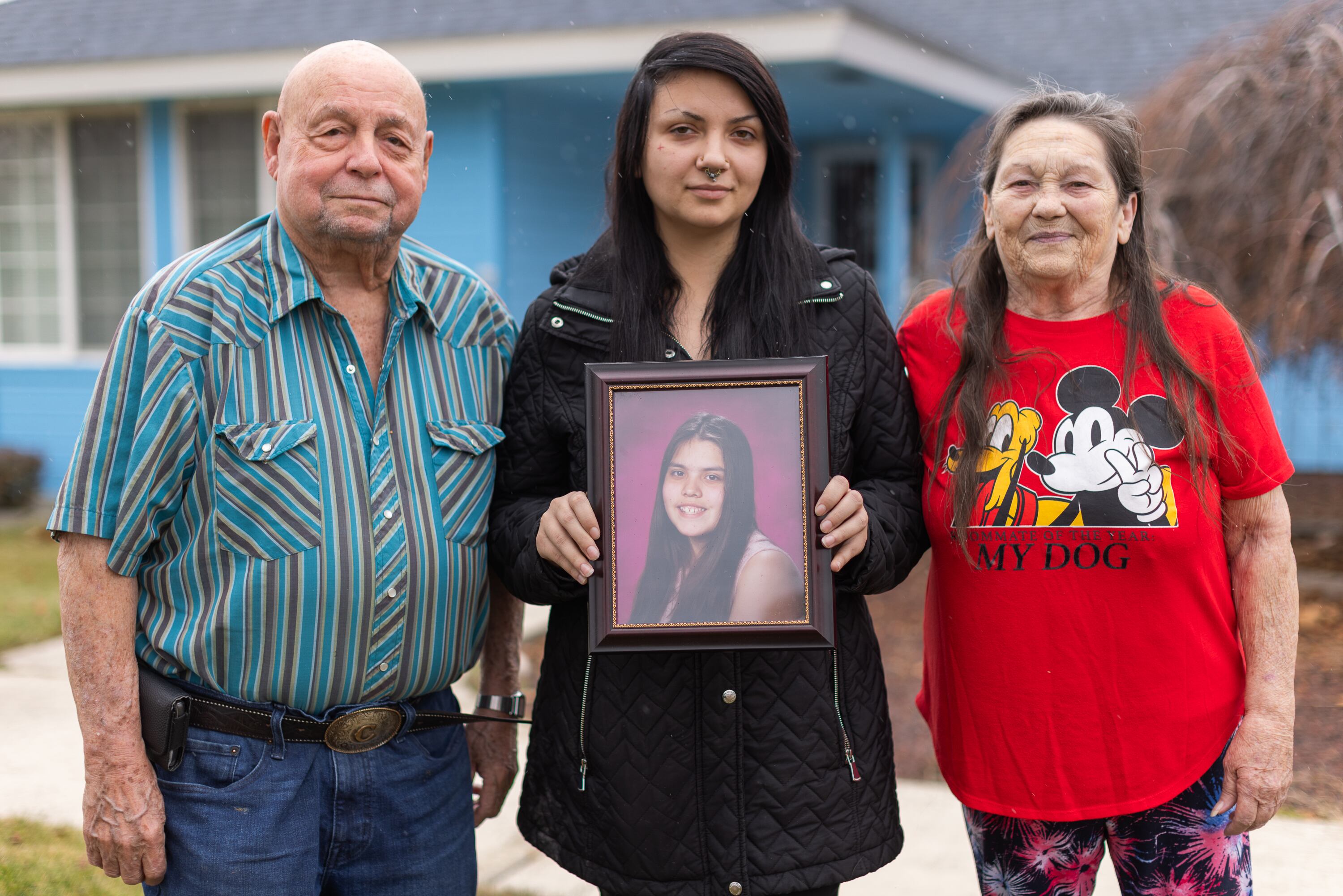 From left, Charlie, Charlotte and Bonnie Groo stand outside the home where Kit Nelson-Mora was raised in Yakima, Wash. Charlotte holds a photo of Kit, who went missing at age 16.
