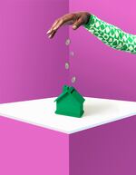 Studio photo of a hand dropping pound coins into a tiny green piggy bank-shaped like a house.  