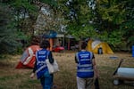 Two people walk in a wooded park with tents