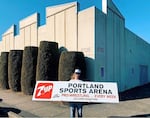 A man with long blond hair and wearing a white and blue baseball cap holds up a large sign. The sign reads "Portland Sports Arena Pro-Wrestling ... Every Week"