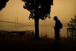 A person rides a skateboard along the Willamette River as smoke from wildfires partially obscures the Tilikum Crossing Bridge, Saturday, Sept. 12, 2020, in Portland, Ore.