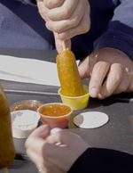 Close-up of a customer's hands dipping a corn dog into a small container of mustard.