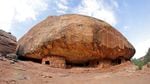 A giant rock with dwellings underneath with blue sky above.